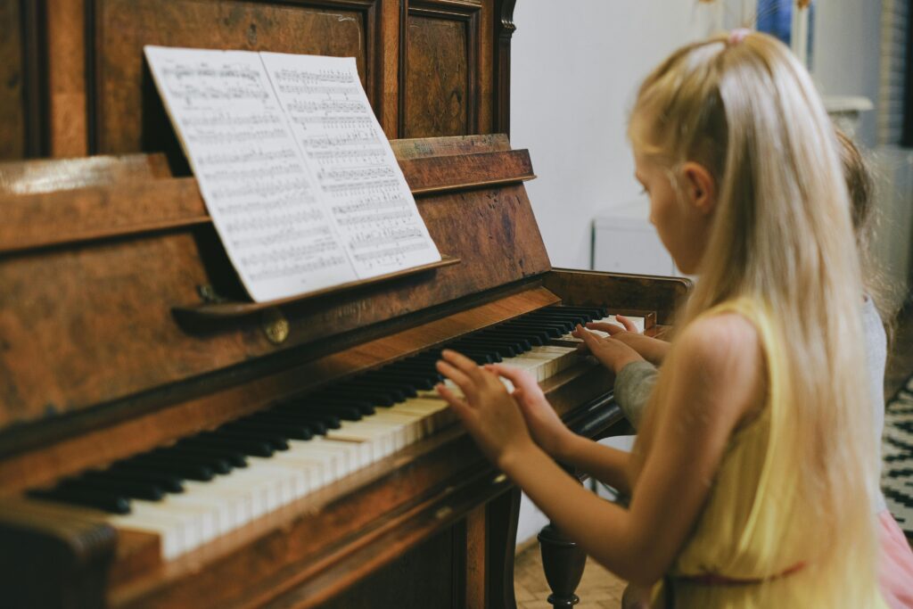 Two young girls playing piano together indoors, focused on a music sheet.