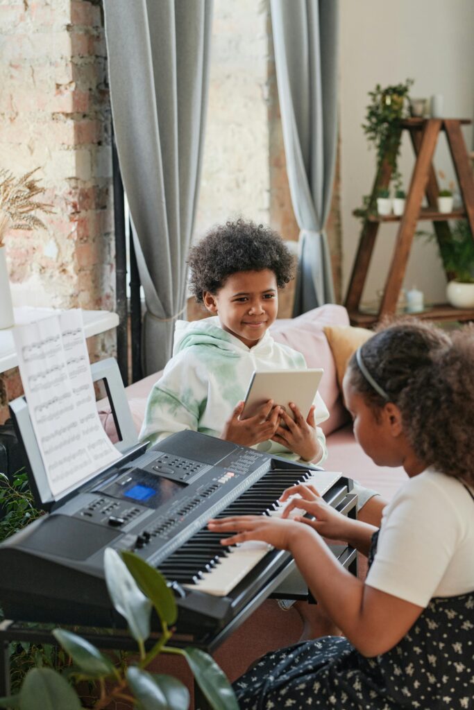 Two kids playing keyboard and tablet in a cozy room setting, showcasing musical talent.