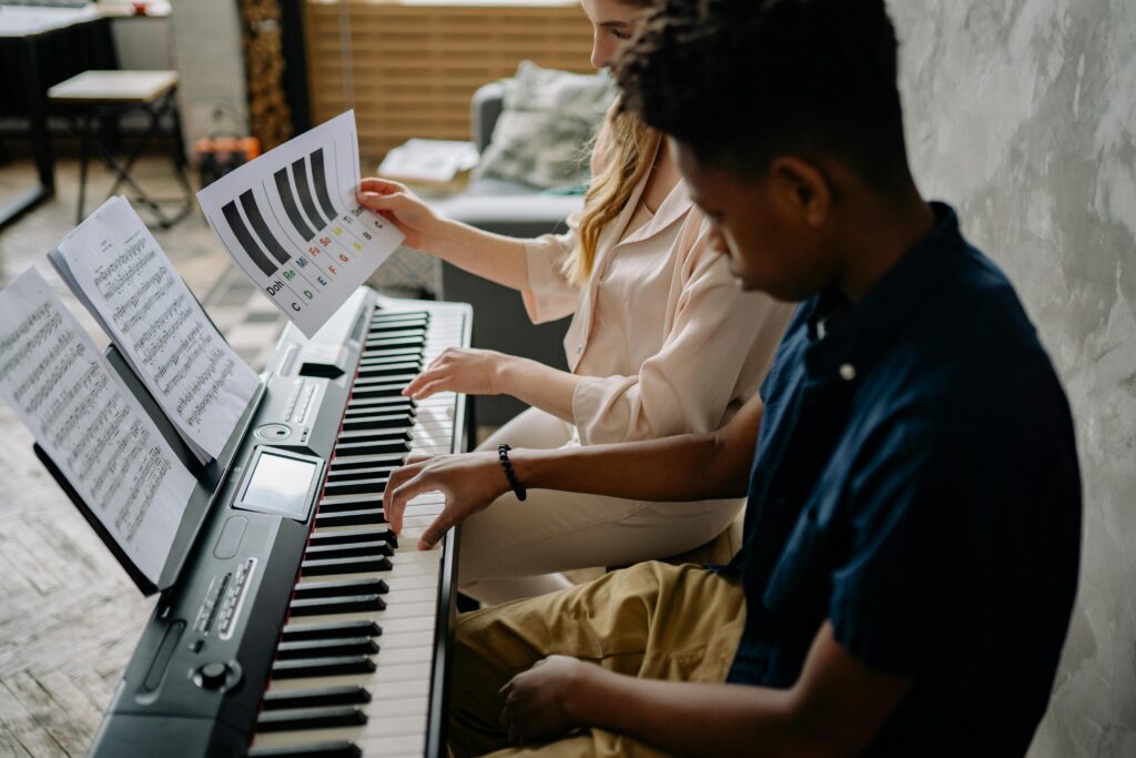 A young boy learns piano with a female teacher, engaging in a music lesson indoors.